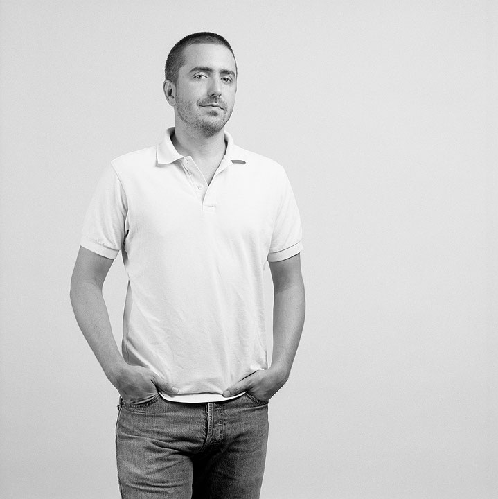 Photographie en noir et blanc de David Altmejd, debout les mains dans les poches, vêtu d’un polo clair à manches courtes et d’une paire de jeans. Il sourit légèrement à l’objectif. (Afficher en plein écran)