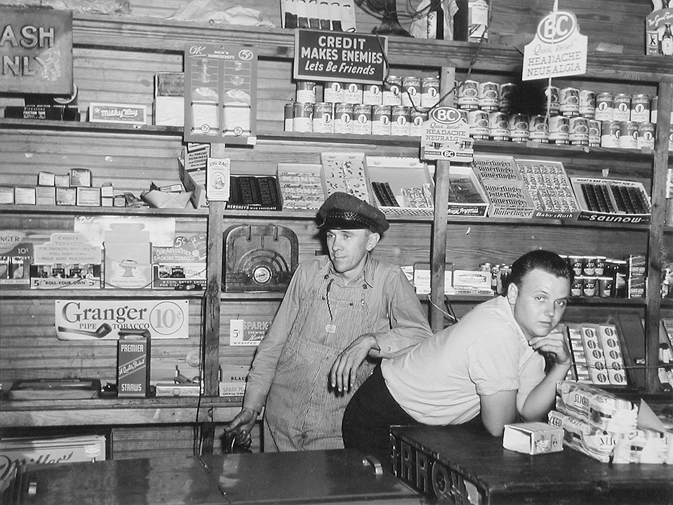 Photo de l’œuvre Interior of Mr Coley’s Store, Mr Coley is Standing with his Helper, Stem, Granville County, North Carolina, May 1940 de Jack Delano (Afficher en plein écran)