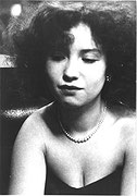 Photographie en noir et blanc d’une jeune femme aux cheveux frisés portant une robe bustier et un collier de perles.