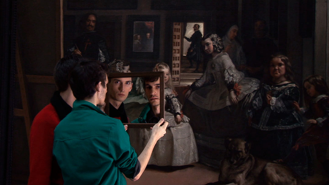Image couleur présentant deux jeunes hommes, vus de dos, devant la peinture Les Ménines de Diego Vélasquez. Ils tiennent un miroir et fixent le spectateur. (Afficher en plein écran)