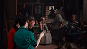 Image couleur présentant deux jeunes hommes, vus de dos, devant la peinture Les Ménines de Diego Vélasquez. Ils tiennent un miroir et fixent le spectateur.