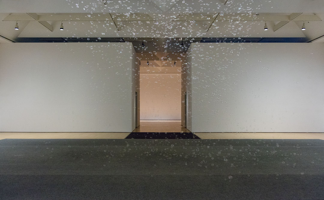 Photographie couleur d’une salle d’exposition dans laquelle de petites bulles descendent du plafond. (Afficher en plein écran)